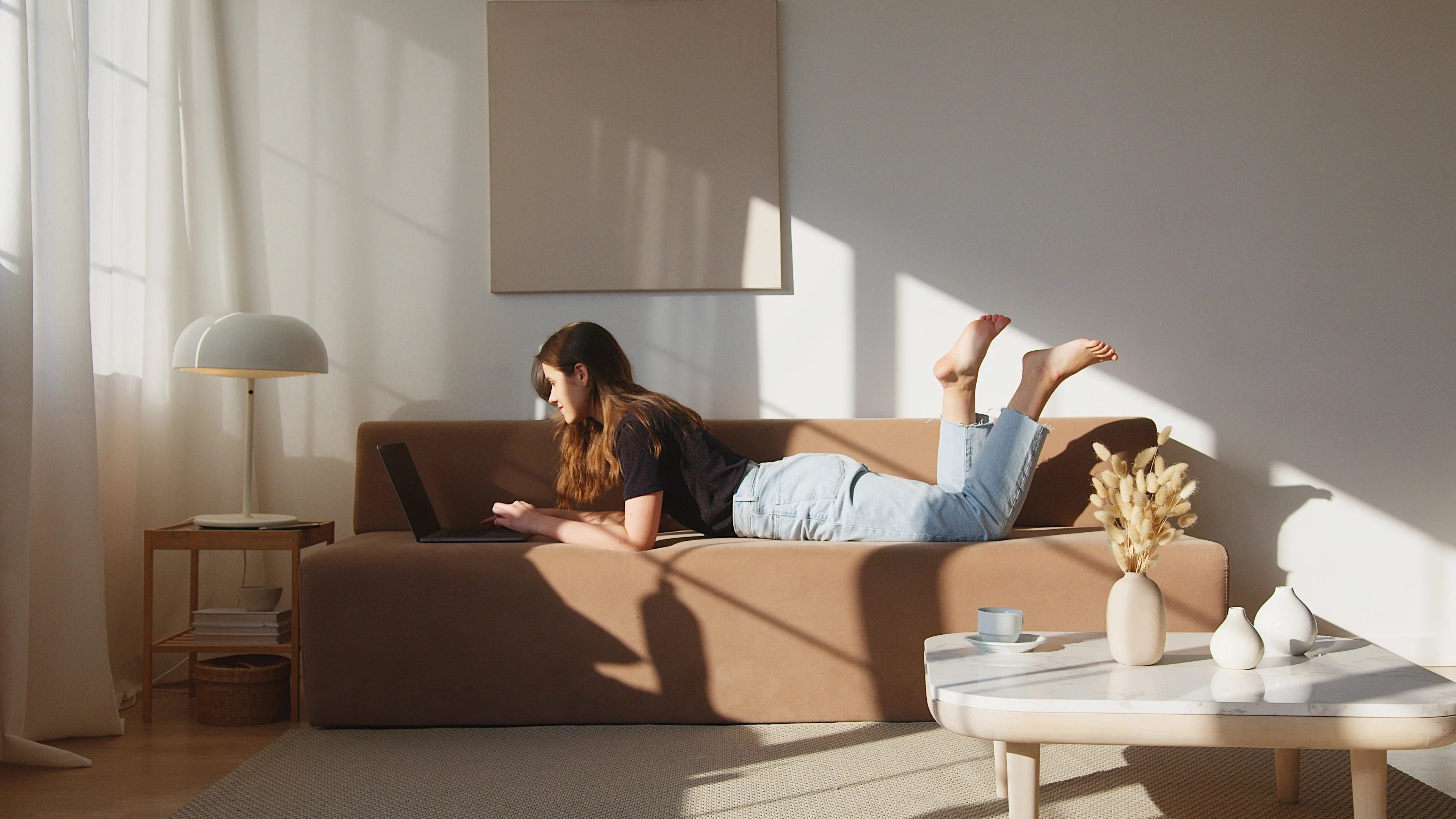 mujer tumbada en el sofa tranajando en el portatil